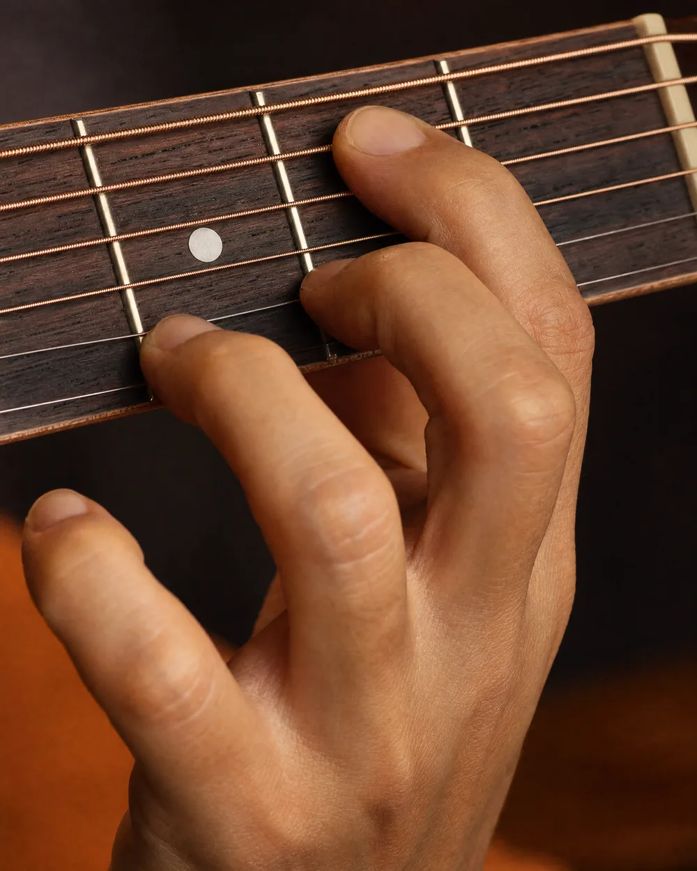 Hand die een akkoord grijpt op de hals van een akoestische gitaar tijdens gitaarles