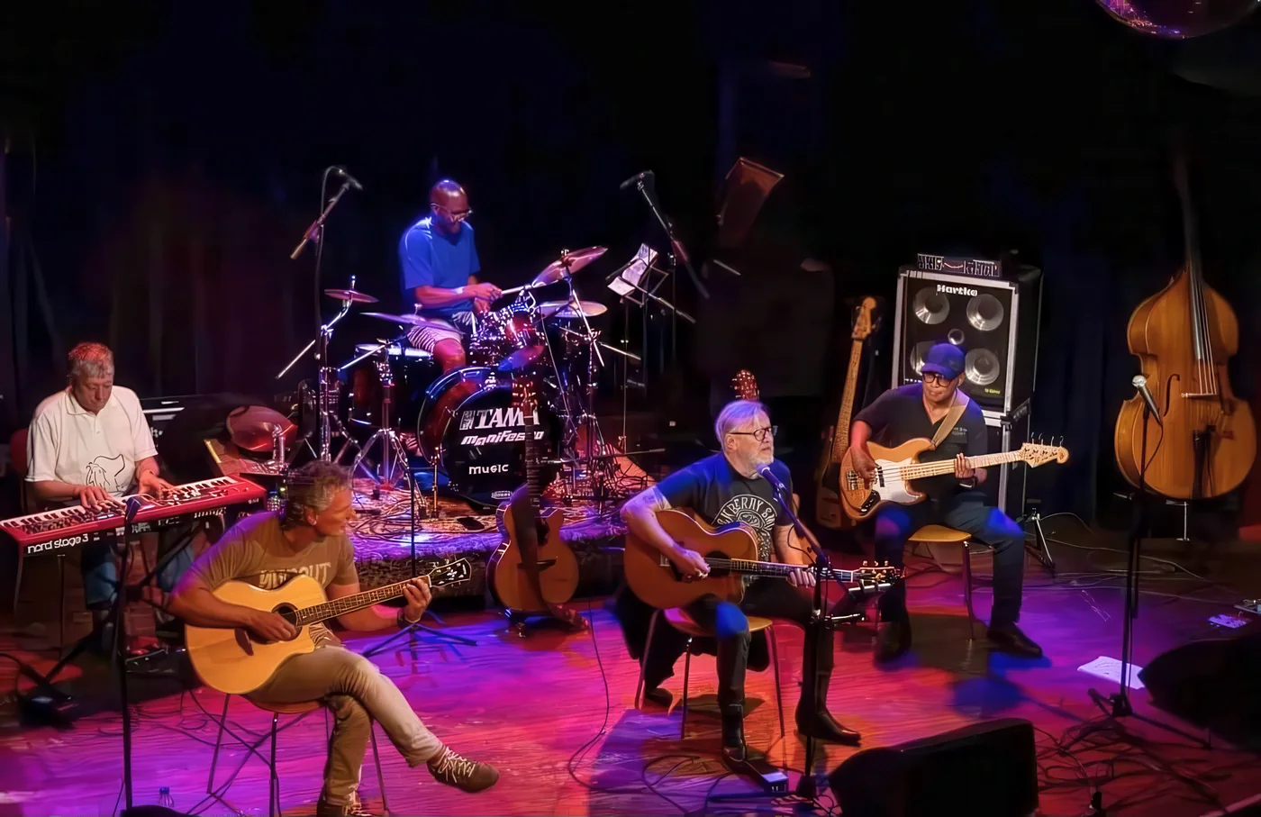 Muzikanten met akoestische gitaren, toetsen, drums en bas op het podium tijdens The Unplugged Session