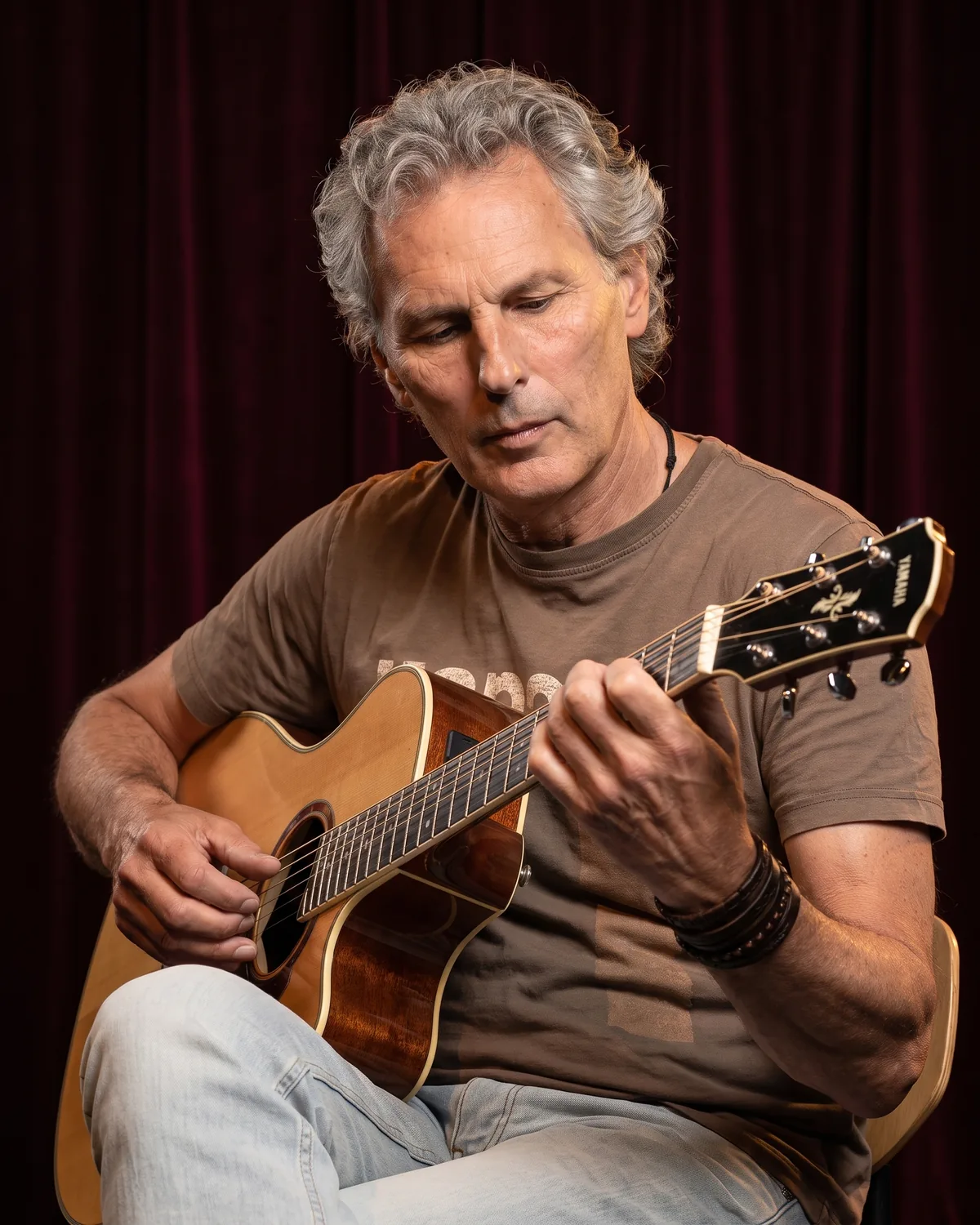 Wim Kingma kijkt naar zijn linkerhand terwijl hij een akkoord grijpt op zijn akoestische gitaar